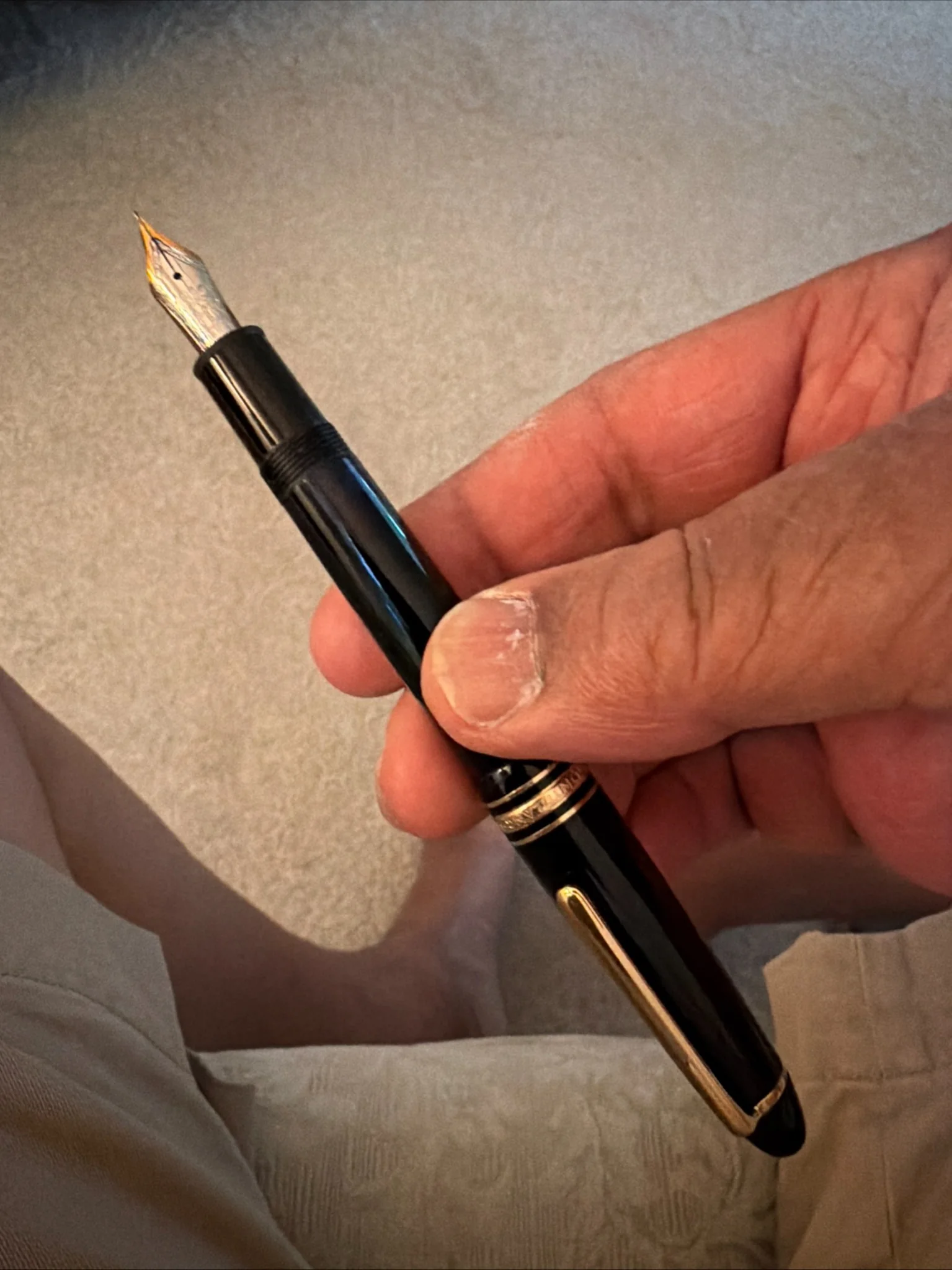 Black fountain pen with gold-tone trim held in hand with the nib exposed